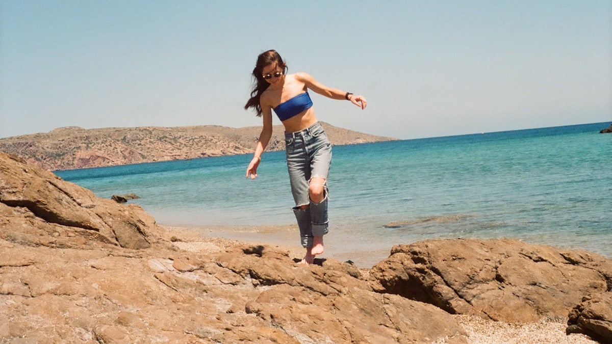 A woman in a bikini jumping off a rock into the ocean