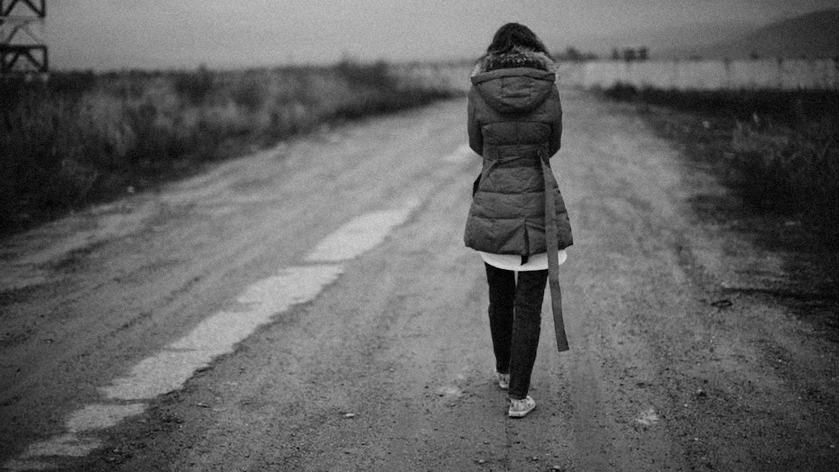a woman walking down a dirt road in the rain
